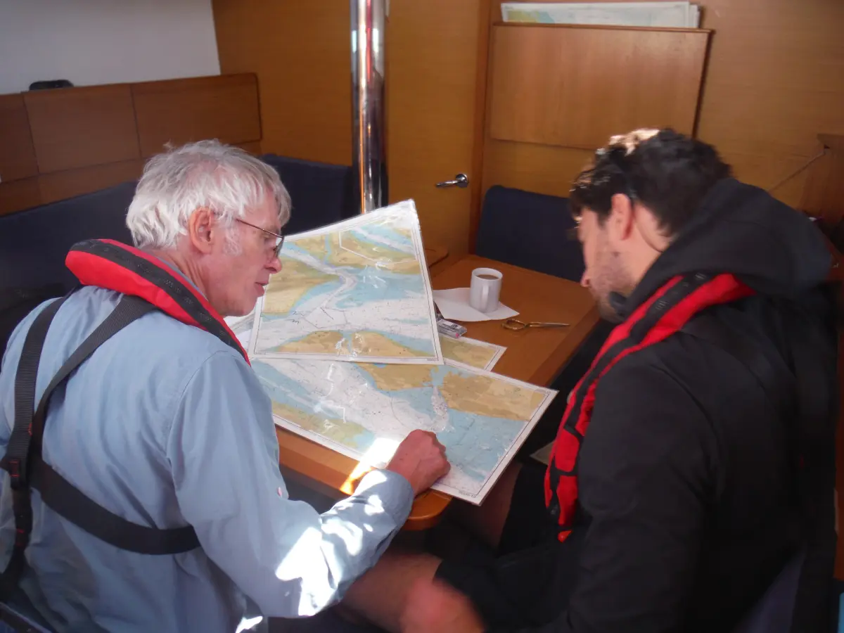 Crew plotting Channel Triangle route on a nautical chart in the saloon